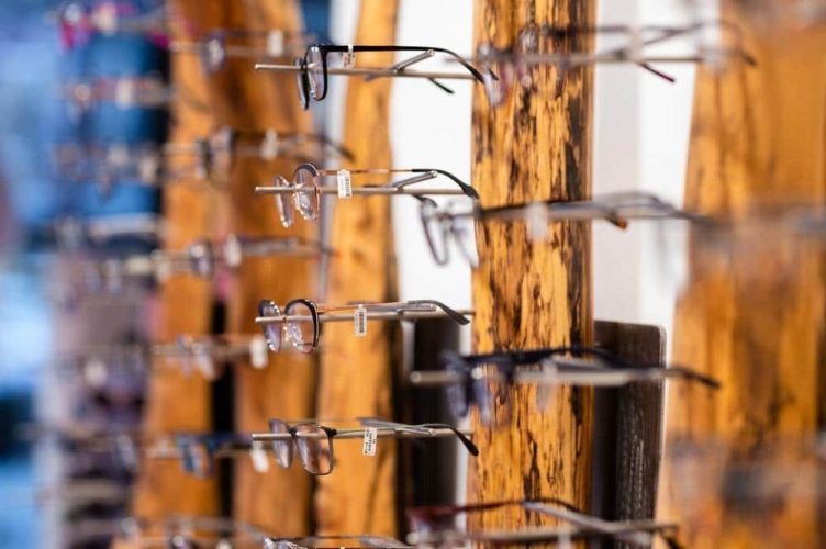 Brillengestelle ausgestellt an rustikalen, naturbelassenen Holzständern in einem Optikergeschäft.